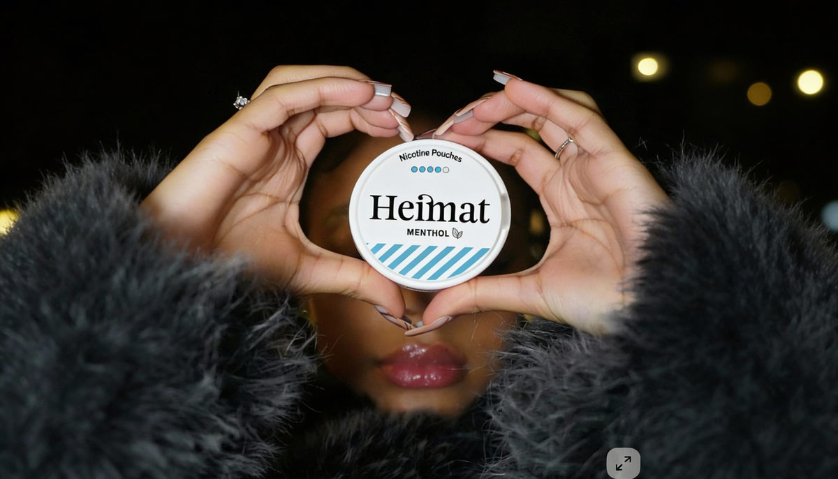 Heimat Menthol Nicotine Pouches dozė širdies formos pakuotėje, laifestailio nuotrauka su moterimi juodame paltje